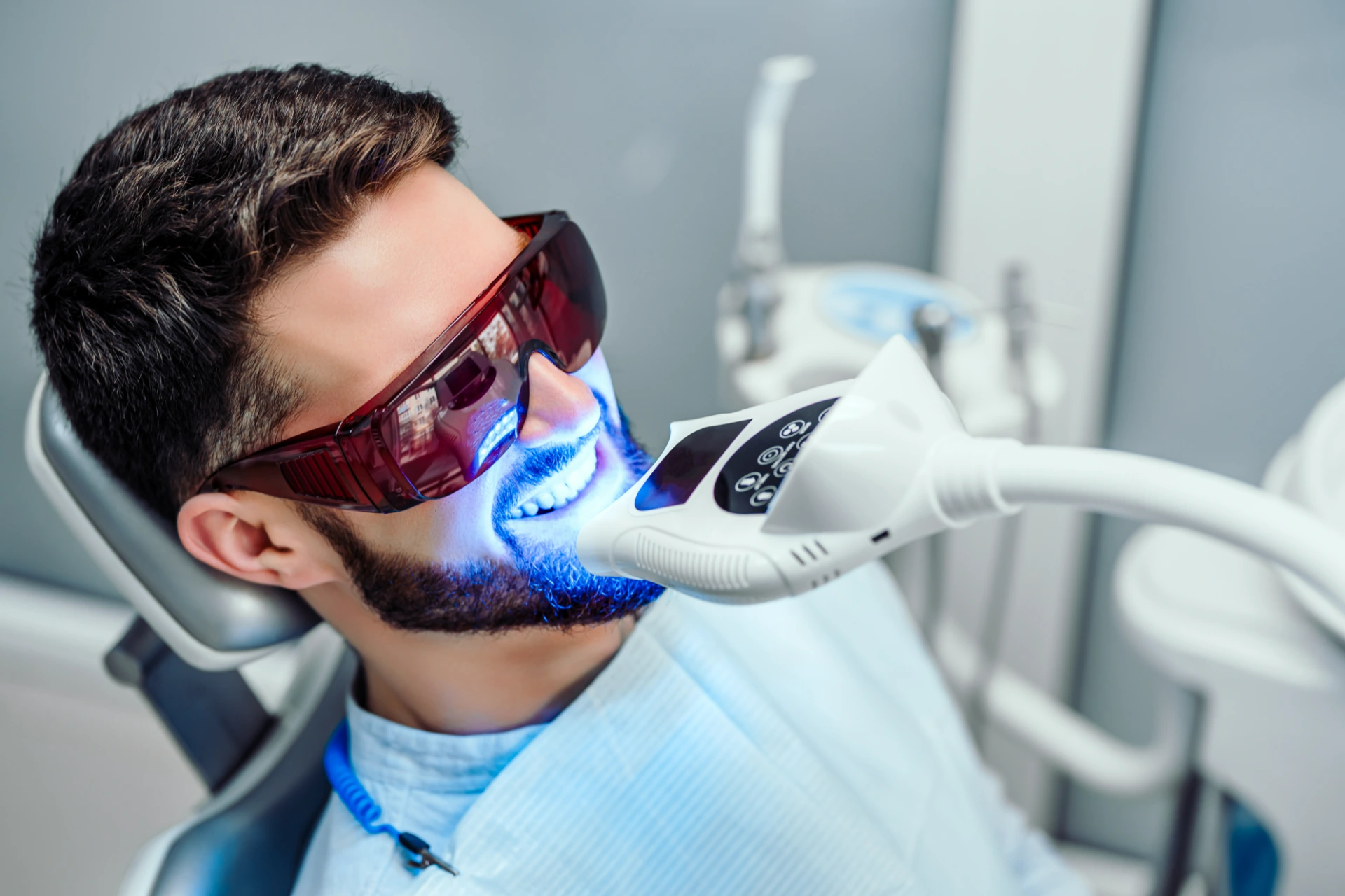 Dentist starting teeth whitening procedure with young man.