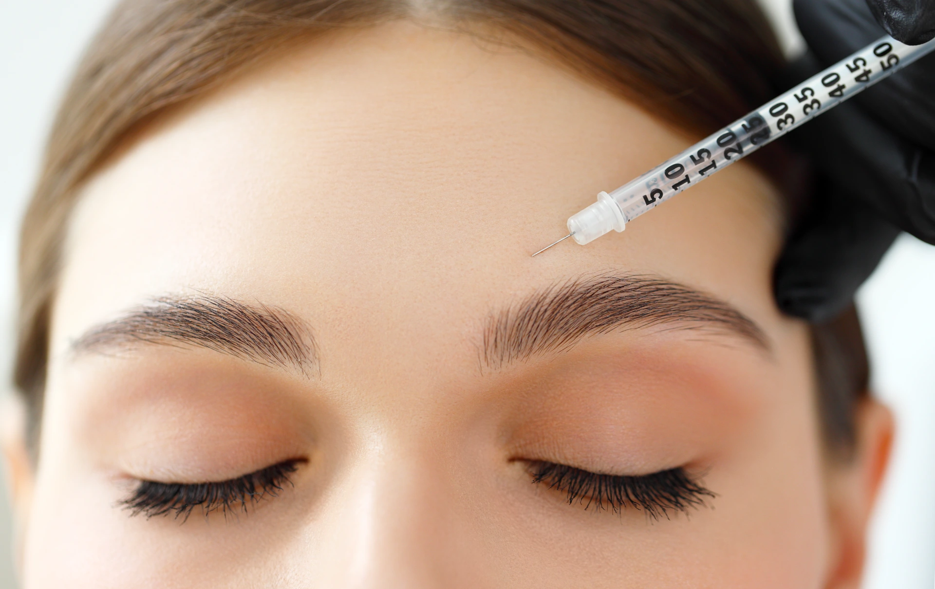 Closeup of crop young female patient receiving injection in the forehead over eyebrow during plastic surgery in modern beauty clinic