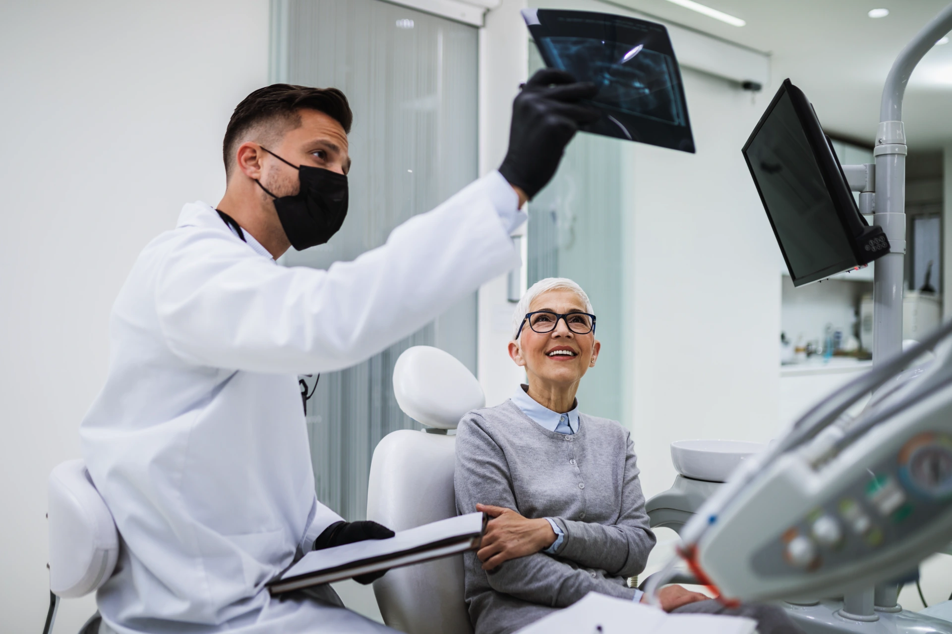 The dentist observes a x-ray image of his patient. Dentist is wearing protective face mask due to coronavirus pandemic.