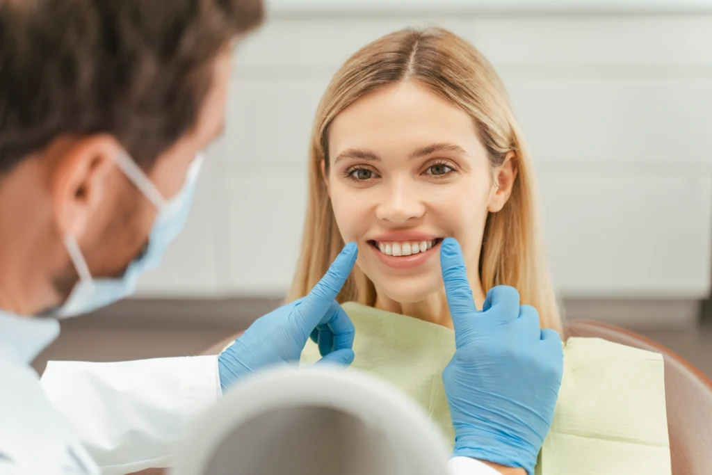 Portrait of attractive young woman with toothy smile sitting in dental chair, dentist checking teeth. Female patient with toothy smile in modern dentistry. Dental care concept